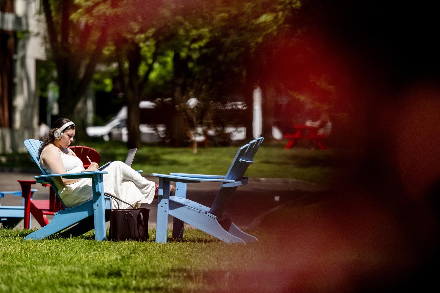 A students sitting in a blue lawn chair writes on a tablet.