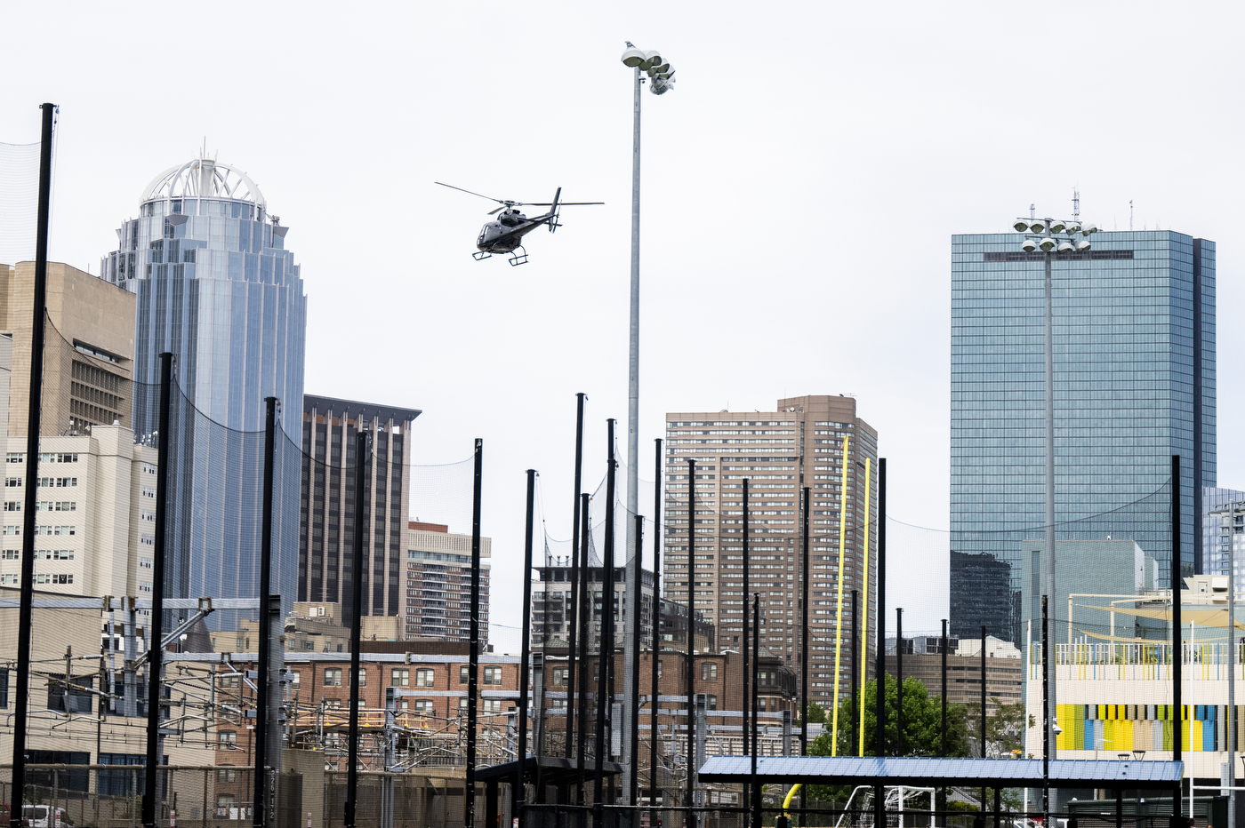 A helicopter flies low above campus with the city skyline in the background.