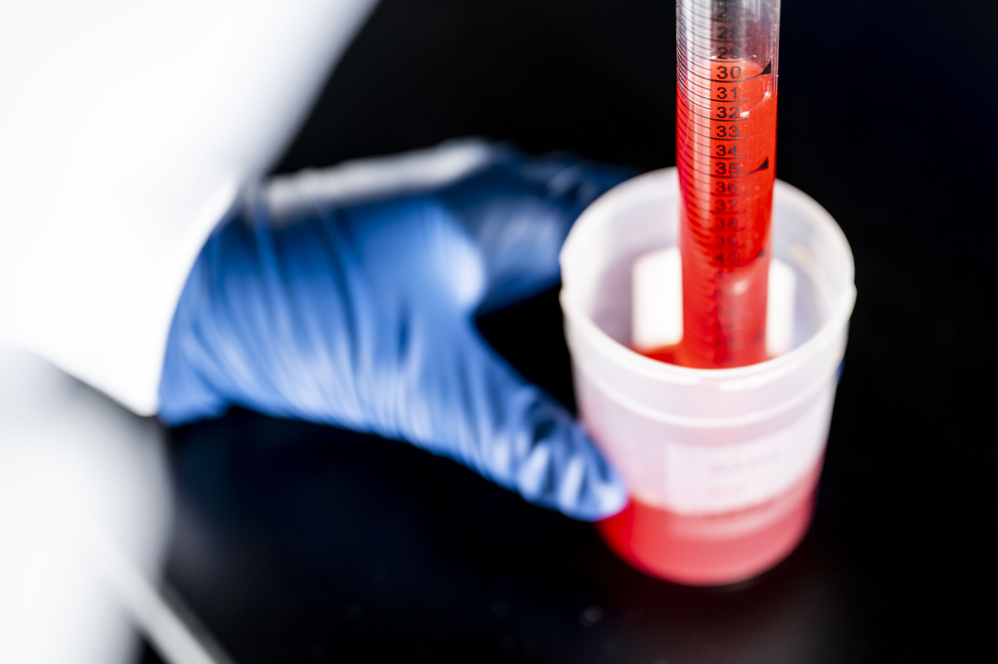 A gloved hand holding a container with red liquid. 