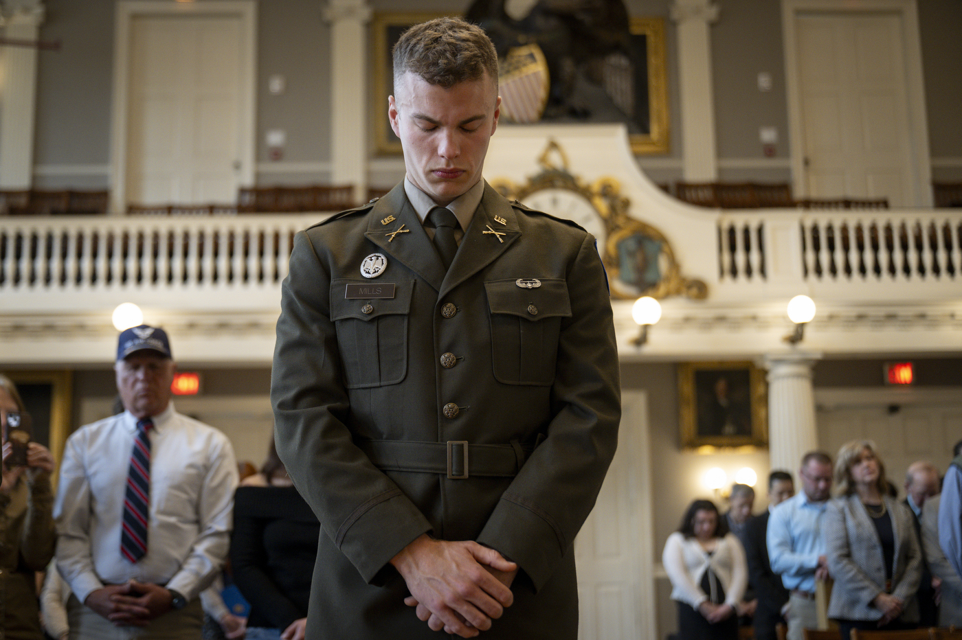 A cadet dressed in military attire bows his head with his arms crossed.
