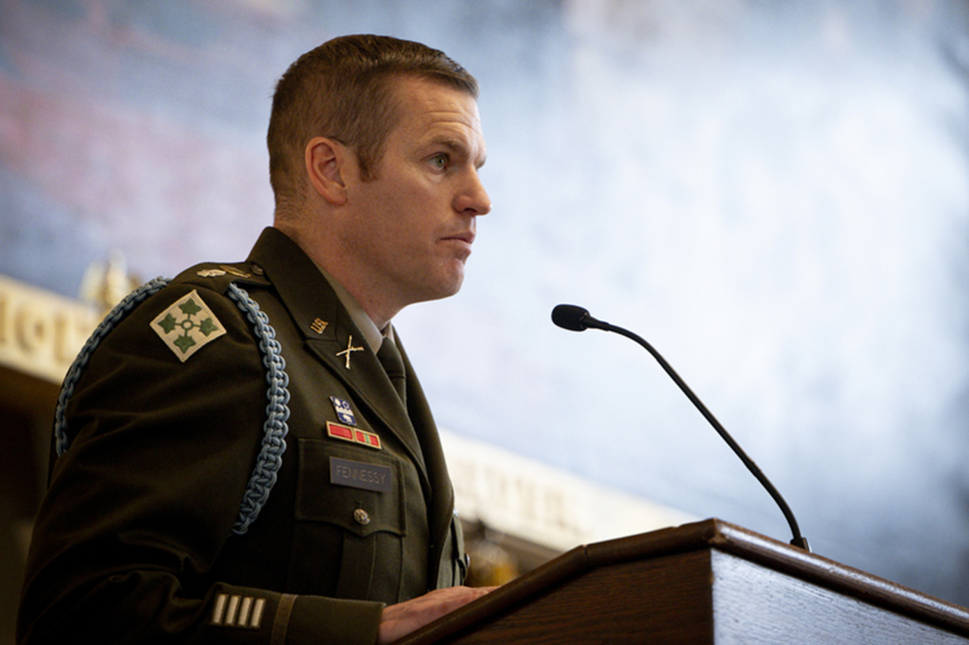 A man dressed in military uniform addresses the crowd at a podium with a microphone.