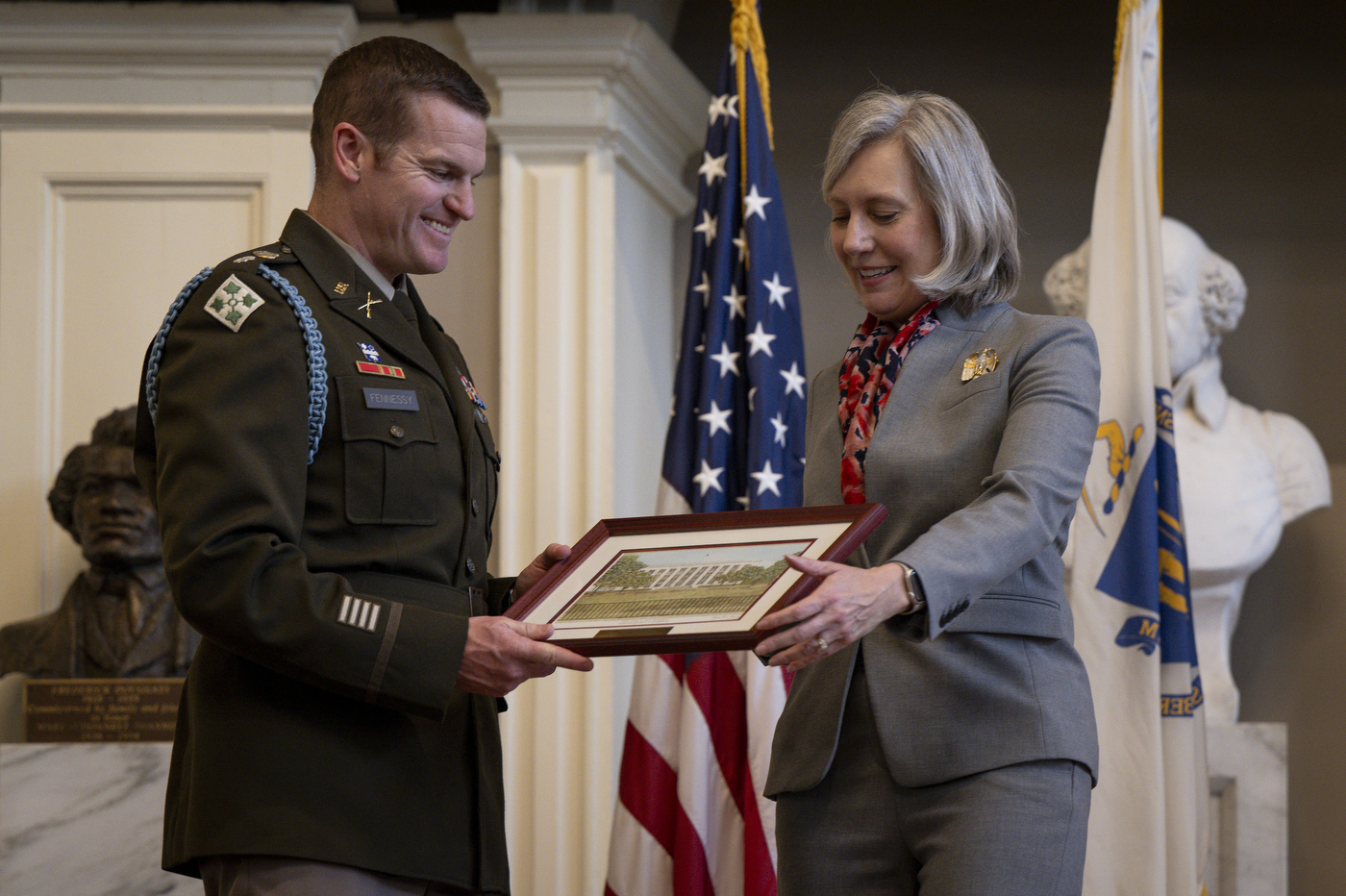 An ROTC member smiles while receiving a framed photo from another person dressed in all gray.