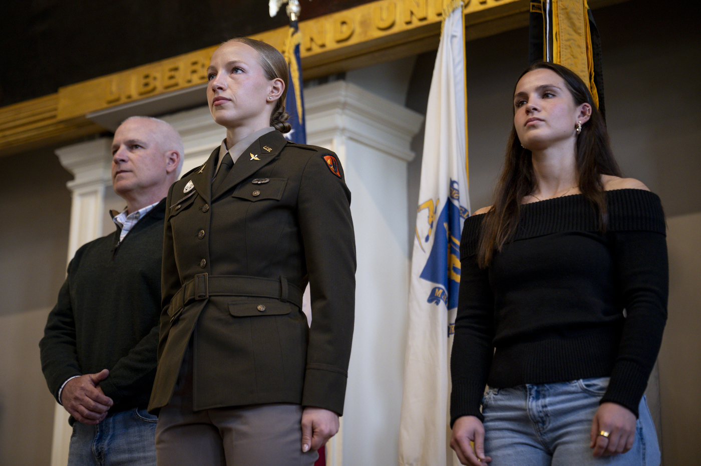 A cadet stands in formation between two people dressed in civilian clothing.