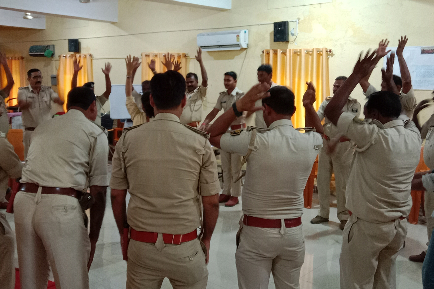 Police officers stand in a circle during a training exercise with their hands raised.