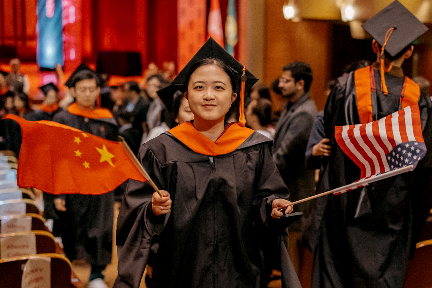 A Northeastern graduate holds a Chinese flag in one hand and an American flag in the other.
