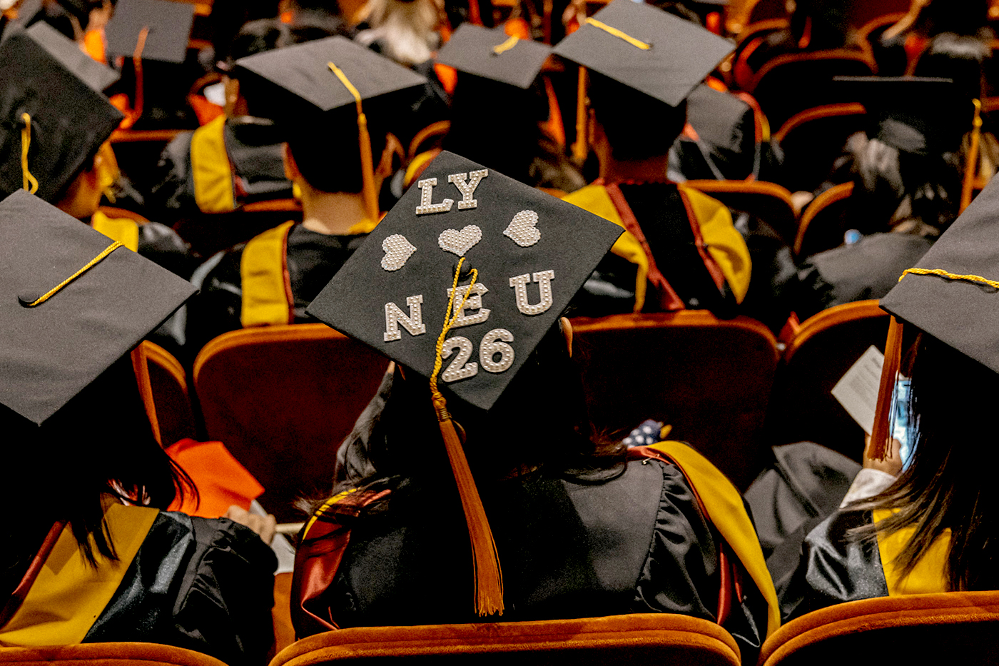 A crowd of graduates sit in the crowd with their caps and gowns.