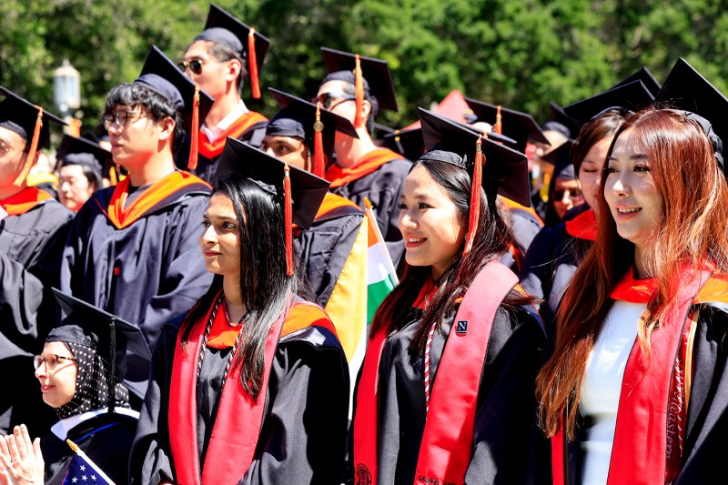Graduates in regalia smile in the sun.