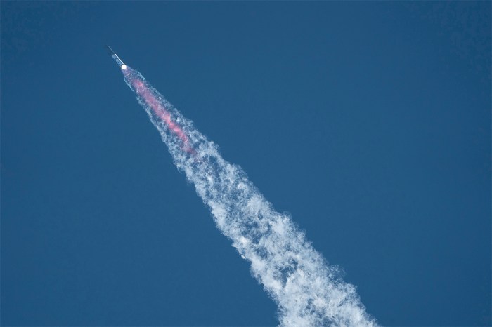 From the ground, SpaceX's Starship rocket 38 launches during the 11th test flight on October 13, 2025 as seen from South Padre Island in Texas. The background is a blue sky with no clouds, as the rocket leaves behind contrails.