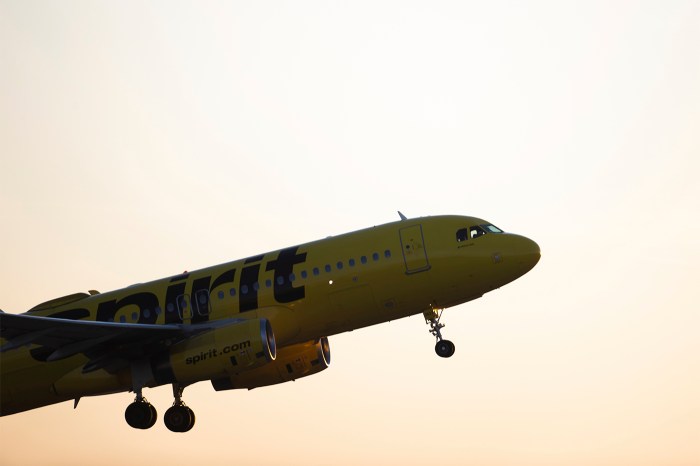 A yellow Spirit Airlines plane in the air against a hazy orange sky background.