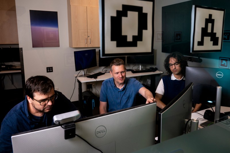 Three people sitting in front of computers discuss observations.