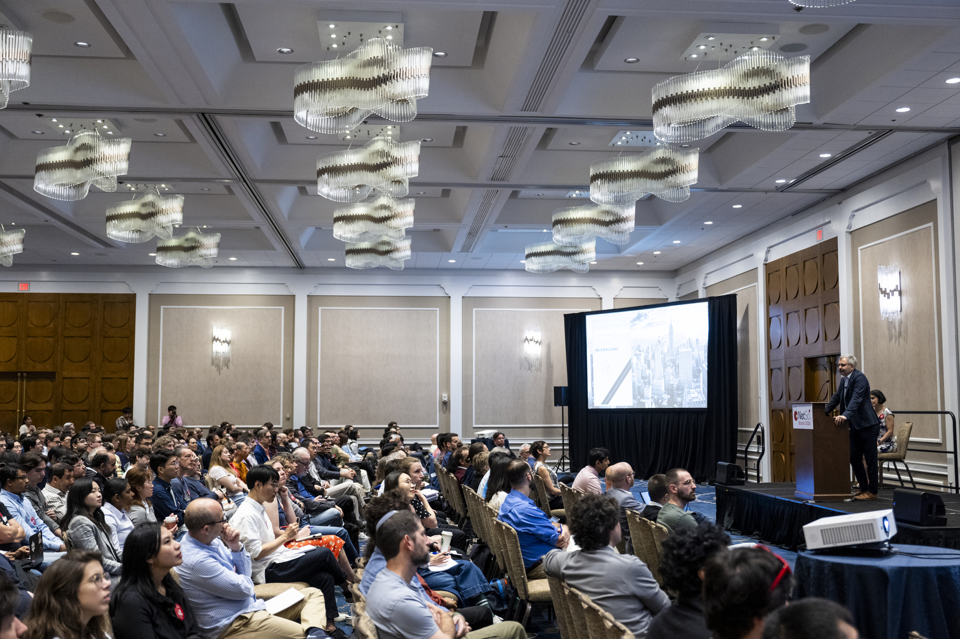 A packed ballroom audience watching a presenter at a podium during NetSci Boston 2026. 