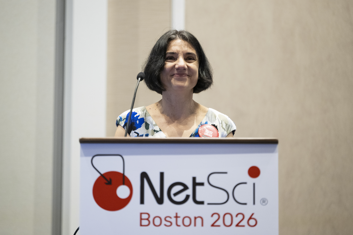 A speaker at the NetSci Boston 2026 podium smiling. 