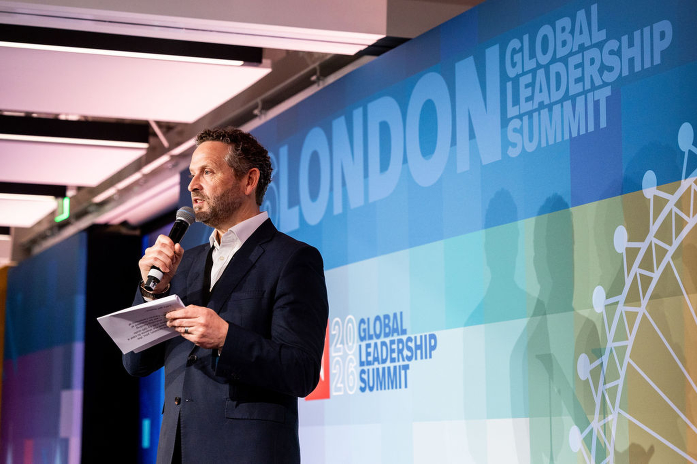 A man speaks at a microphone in front of the London Global Leadership Summit backdrop.