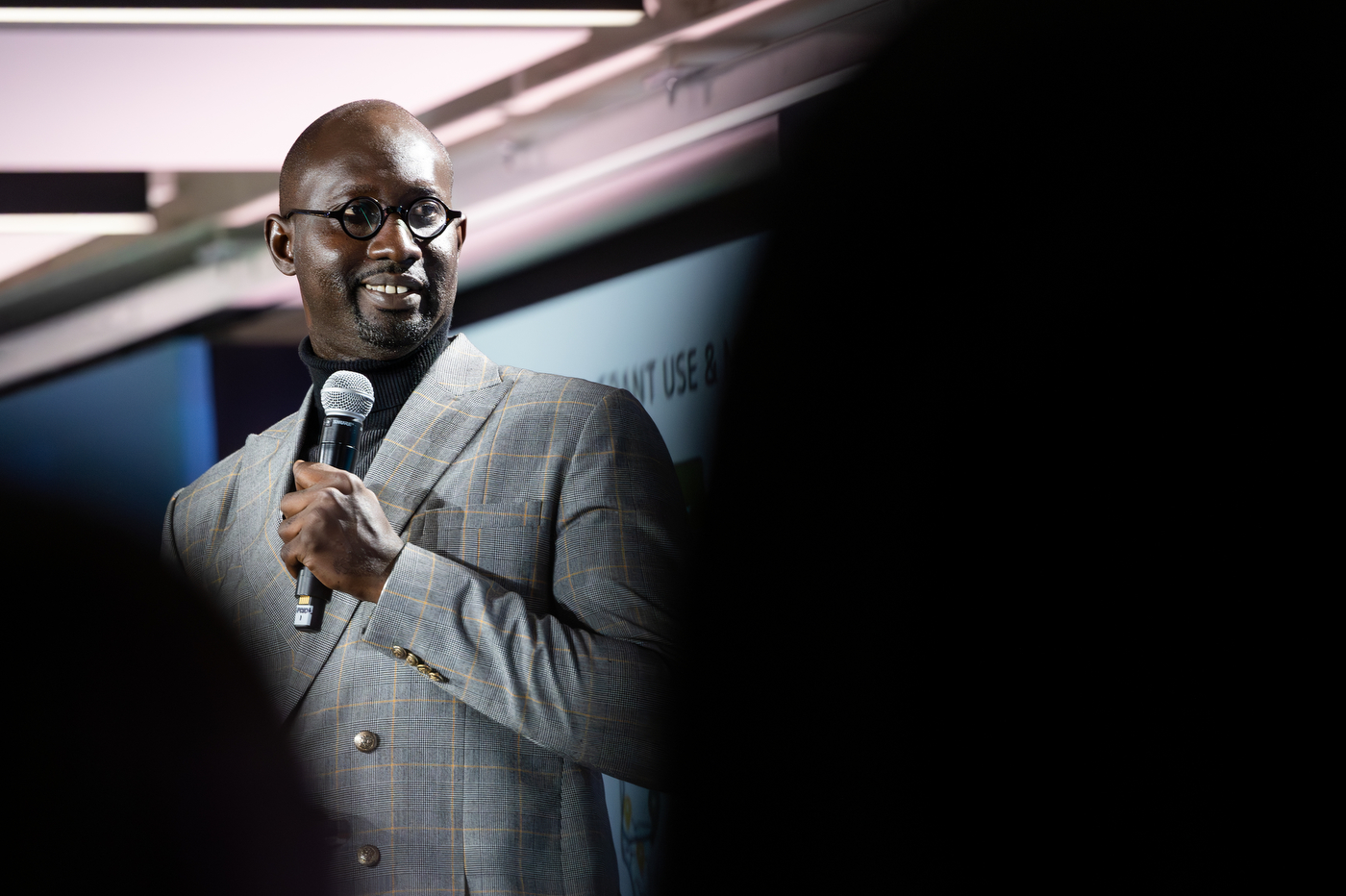 A man in a gray suit speaks at a microphone on stage.