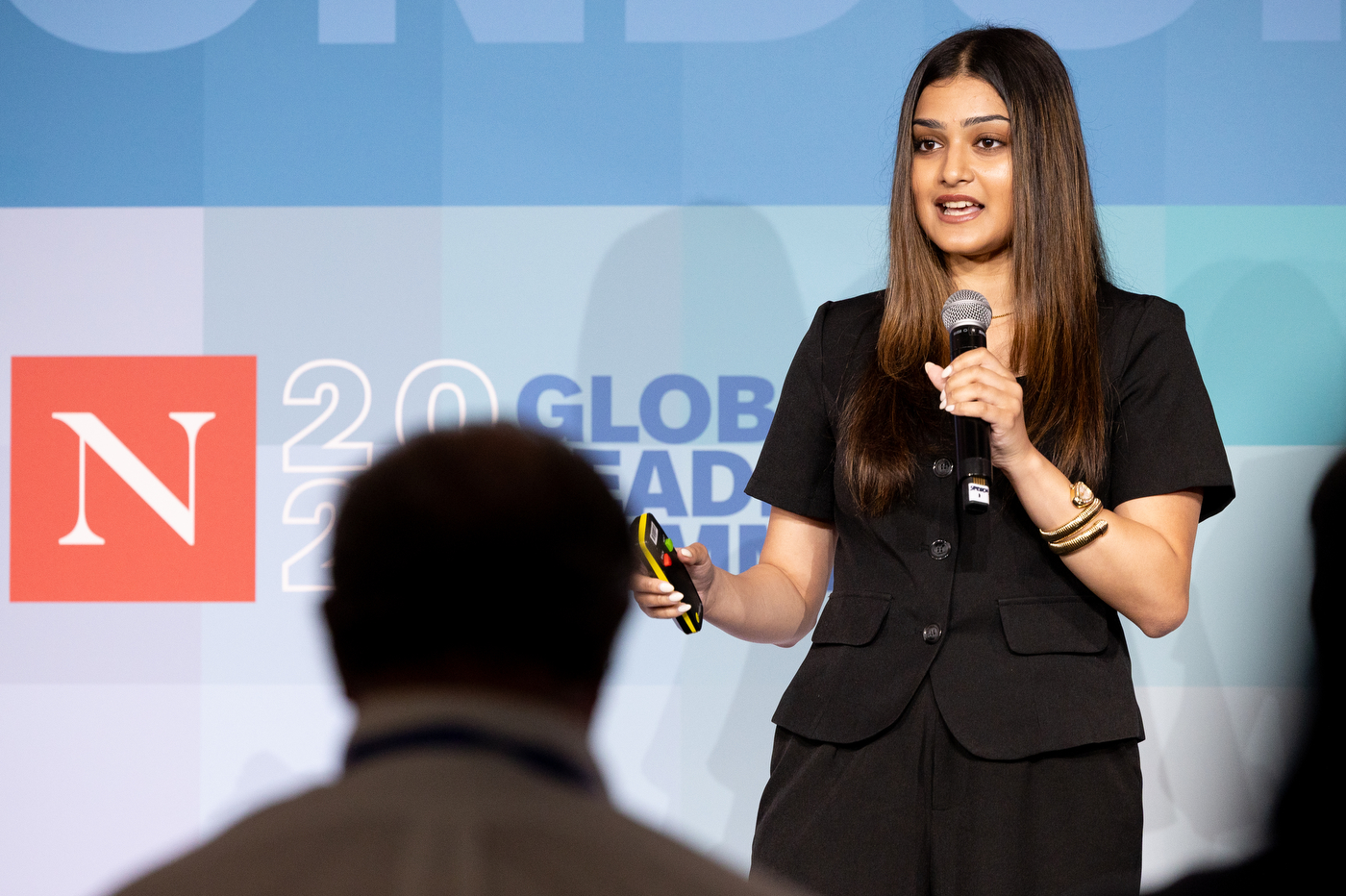 A young woman speaks at a microphone in front of the Northeastern Global Leadership Summit backdrop.