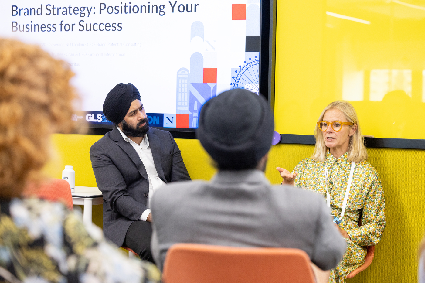 Two panelists address attendees while sitting next to a screen that says 'Brand Strategy: Positioning Your Business for Success' at the Global Leadership Summit. 