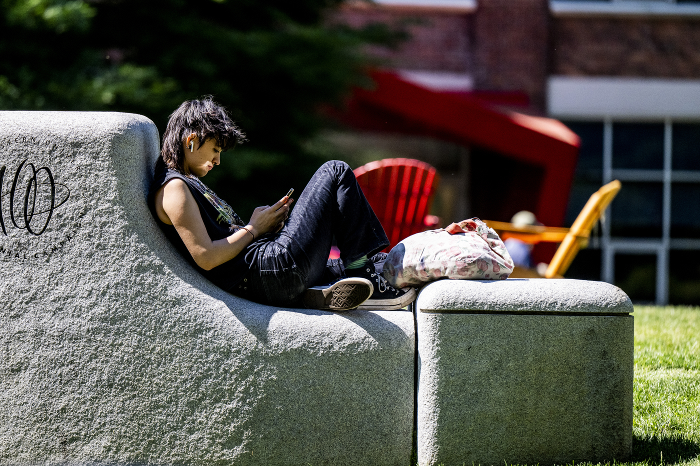 A student reclines on a wall outside while using their phone.