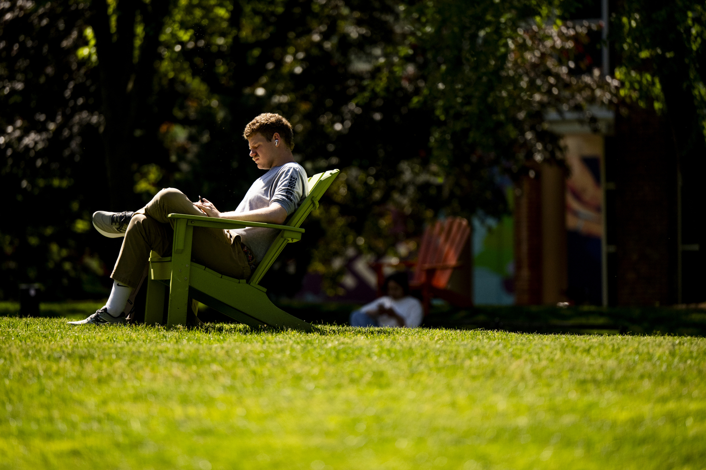A student sits on a lawn chair in a grassy field.