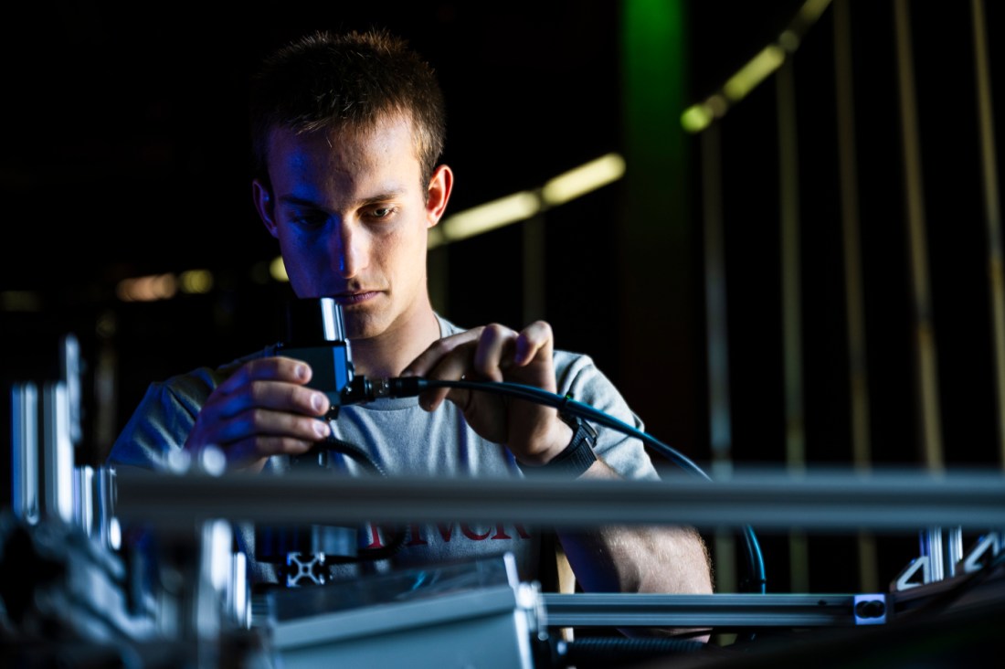 A close up of a Northeastern student's face as he concentrates on machine wiring.