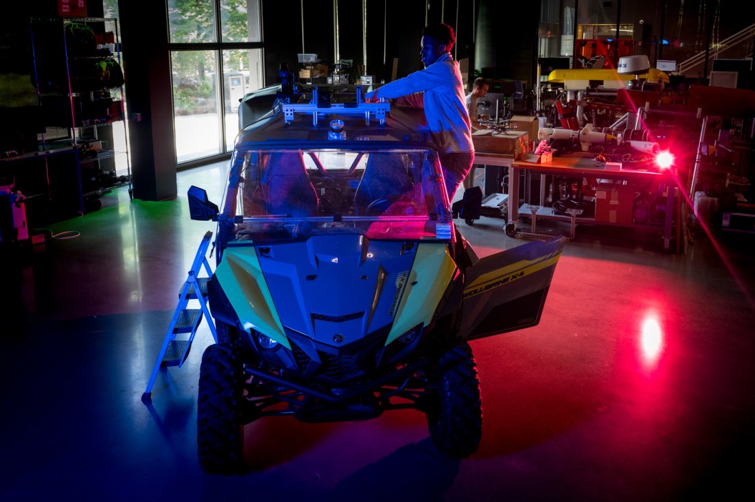James Tukpah stands on the side of a 4 wheel vehicle while working on setting up sensors on top of the car.