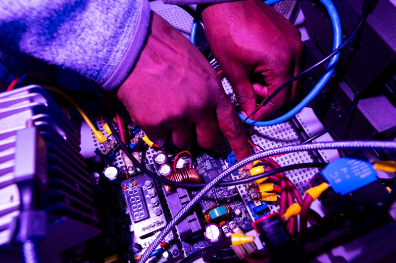 A close up of a student's hands working on the inside of a machine's wiring.