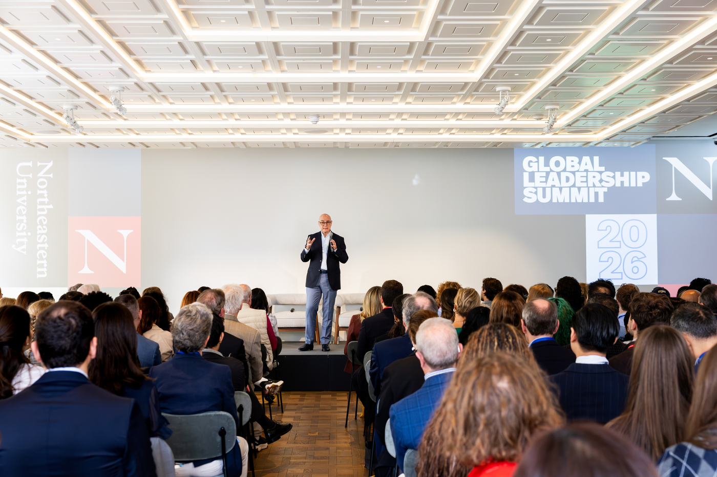 Aoun addresses a seated audience at the Northeastern Global Leadership Summit in London, standing on stage beneath a large event backdrop.