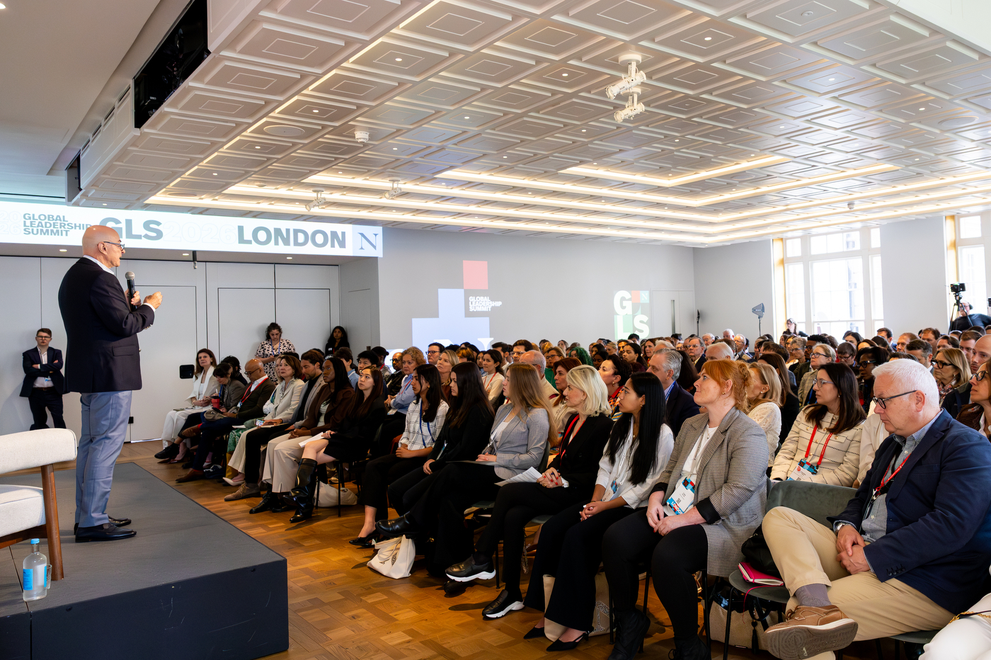 Aoun delivers a keynote presentation to a packed audience at the Northeastern Global Leadership Summit in London, with event branding displayed throughout the conference hall.