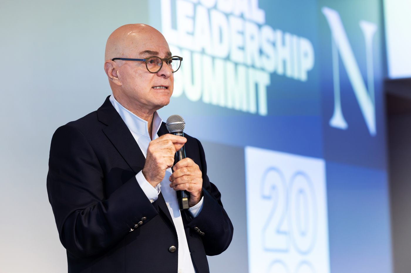 Joseph E. Aoun, president of Northeastern University, speaks into a handheld microphone during the Northeastern Global Leadership Summit in London, discussing human leadership in the age of artificial intelligence.