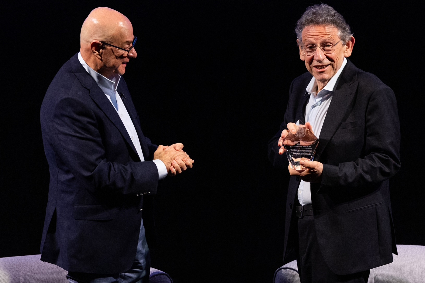 Northeastern President Joseph E. Aoun holds his hands clasped while standing in front of Sir Lucian Grainge, who holds a glass award, on stage at the 2026 Global Leadership Summit in London.