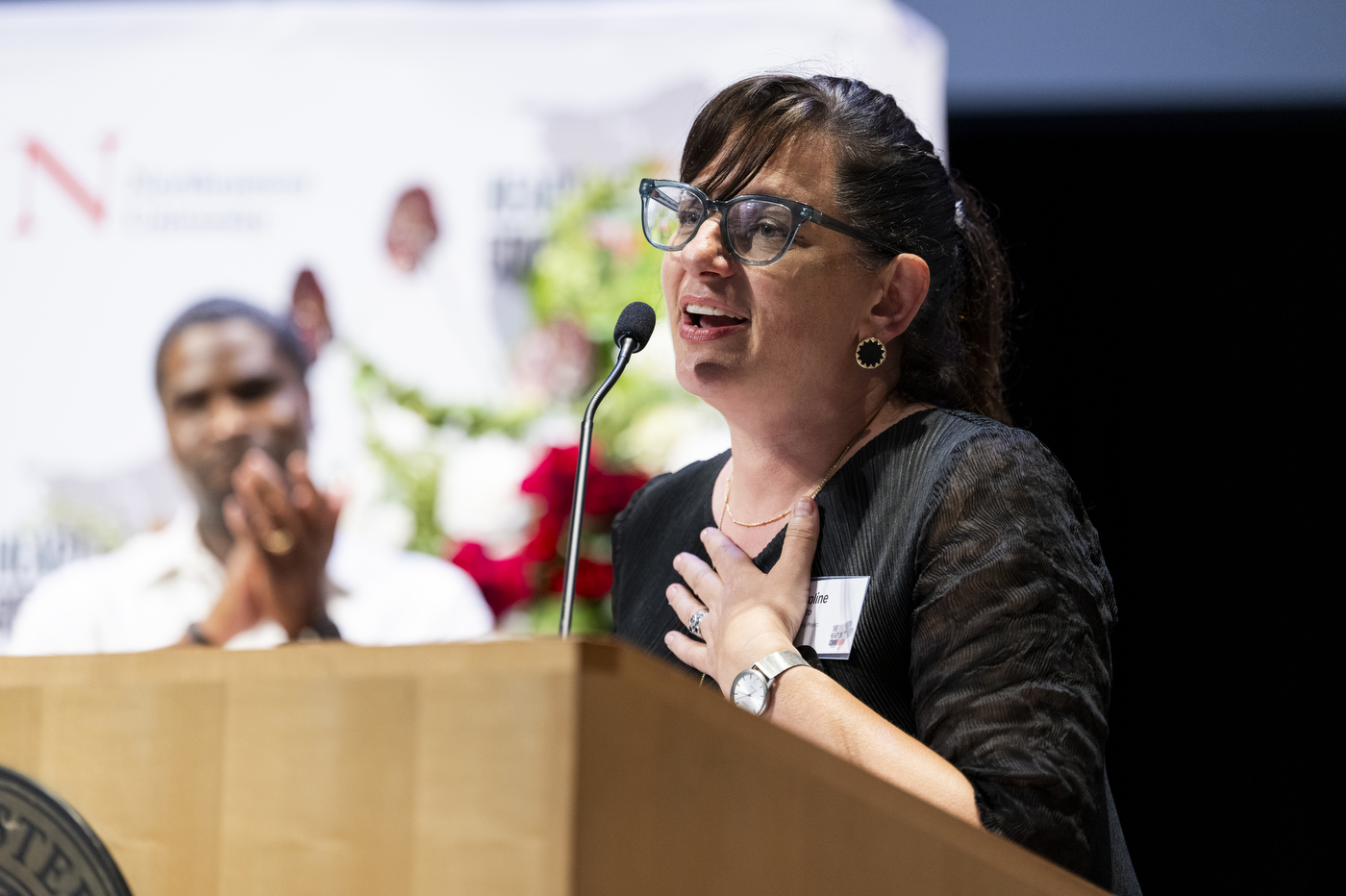 A person in glasses speaks into a mic at a podium.