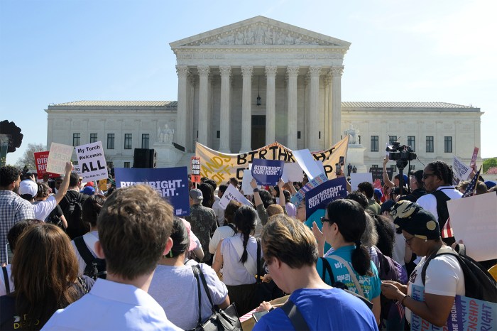 Protestors stand outside the Supreme Court with signs on a sunny day.