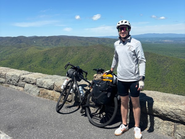 Tim Milich standing next to his bike posing for a photo in front of a green landscape behind him.