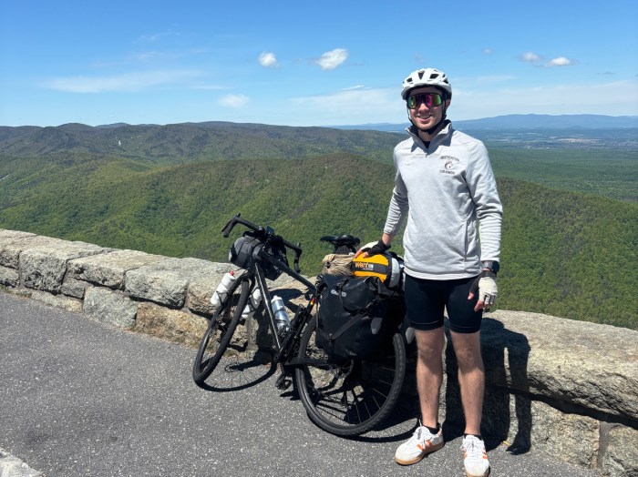 Tim Milich standing next to his bike posing for a photo in front of a green landscape behind him.
