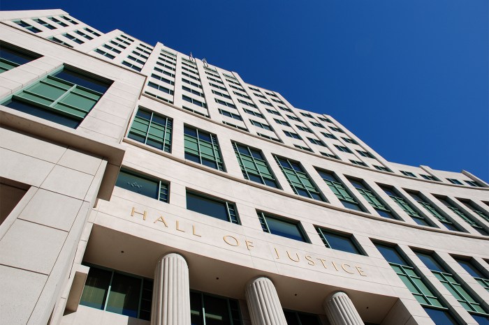 Exterior of a Hall of Justice building, viewed from below against a clear blue sky.
