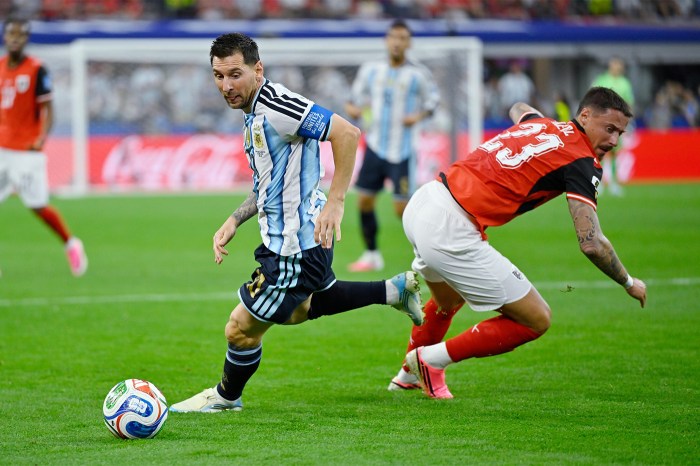 Lionel Messi and Marco Friedl in a physical challenge for the ball during a World Cup match, with Messi pulling ahead.