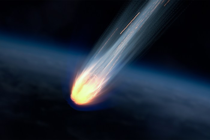 A meteor on fire blazing over earth with a dark sky in the background.