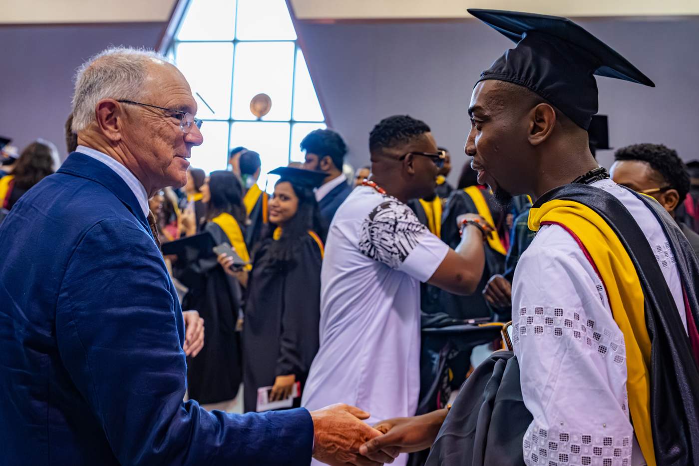 A person wearing a suit and glasses speaks with a graduate at a Northeastern commencement ceremony.