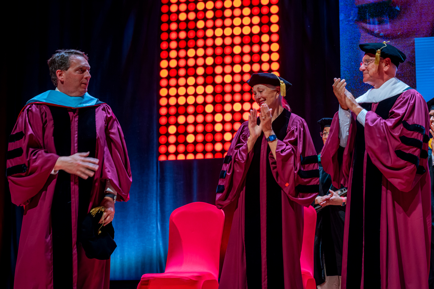 Faculty in doctoral regalia applaud on stage during a Northeastern commencement ceremony.