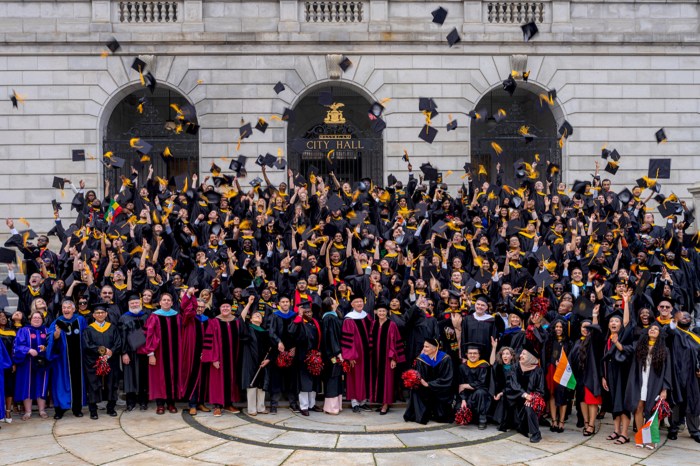 Northeastern University graduates in black and gold regalia toss their caps in the air on the steps of a building in Portland.