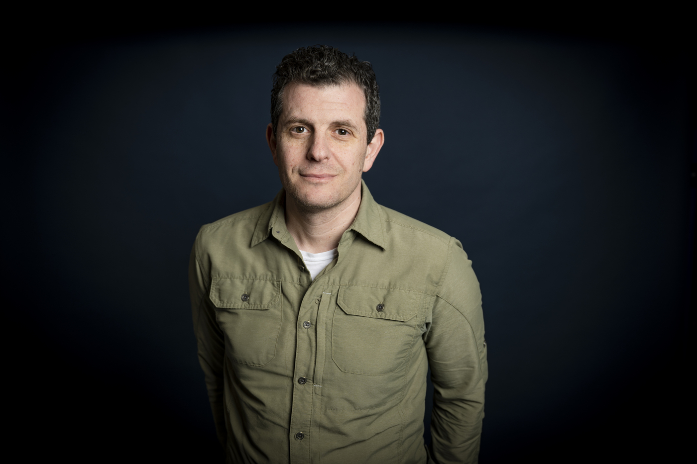 Dennis Staroselsky weairng an olive green button down posing in front of a black background.
