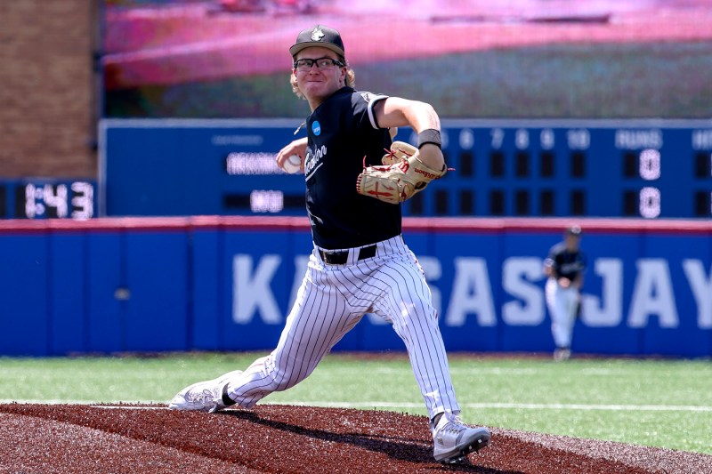 An action photo of a Northeastern player is in the middle of a pitch during a baseball game.