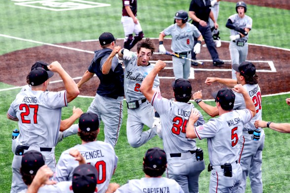 Northeastern Huskies baseball players jump on a teammate at home plate in celebration during an NCAA tournament game.