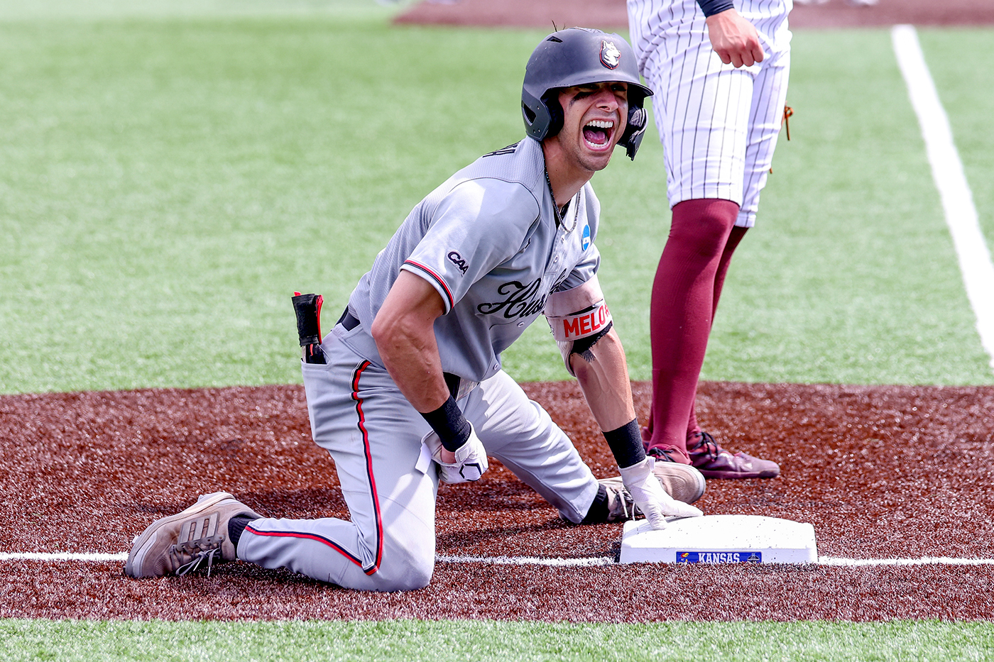 A northeastern player wearing a helmet slide shouts while kneeling on a base mid-game.