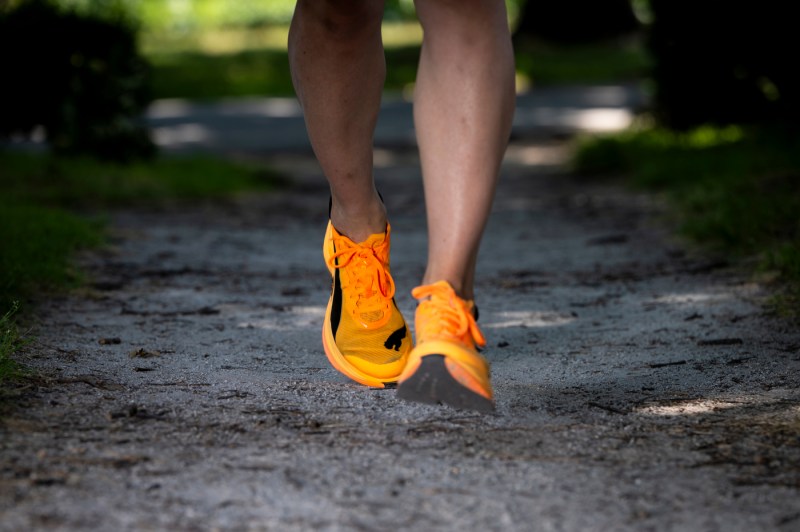  A close up of legs in bright orange running shoes running down a dirt path.