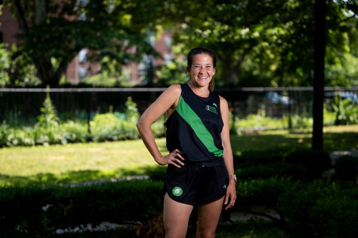 Hannah Rowe is dressed in green and black running attire. She is standing with a hand on her right hip and smiling.