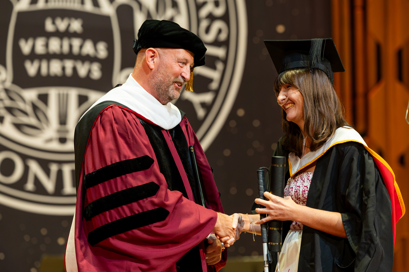 Left: Alexandra shakes hands with a university official in academic regalia on stage as he hands her a diploma case, in front of the Northeastern seal.