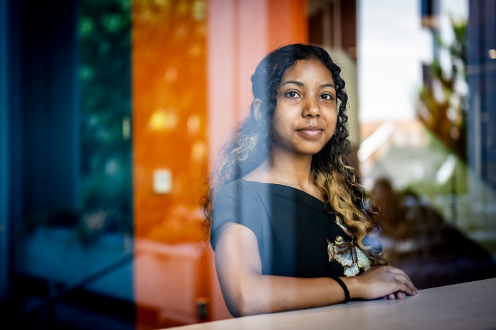 Shashi Murthy wearing a black top, seen inside of a building with warm lighting through the glass of a window.
