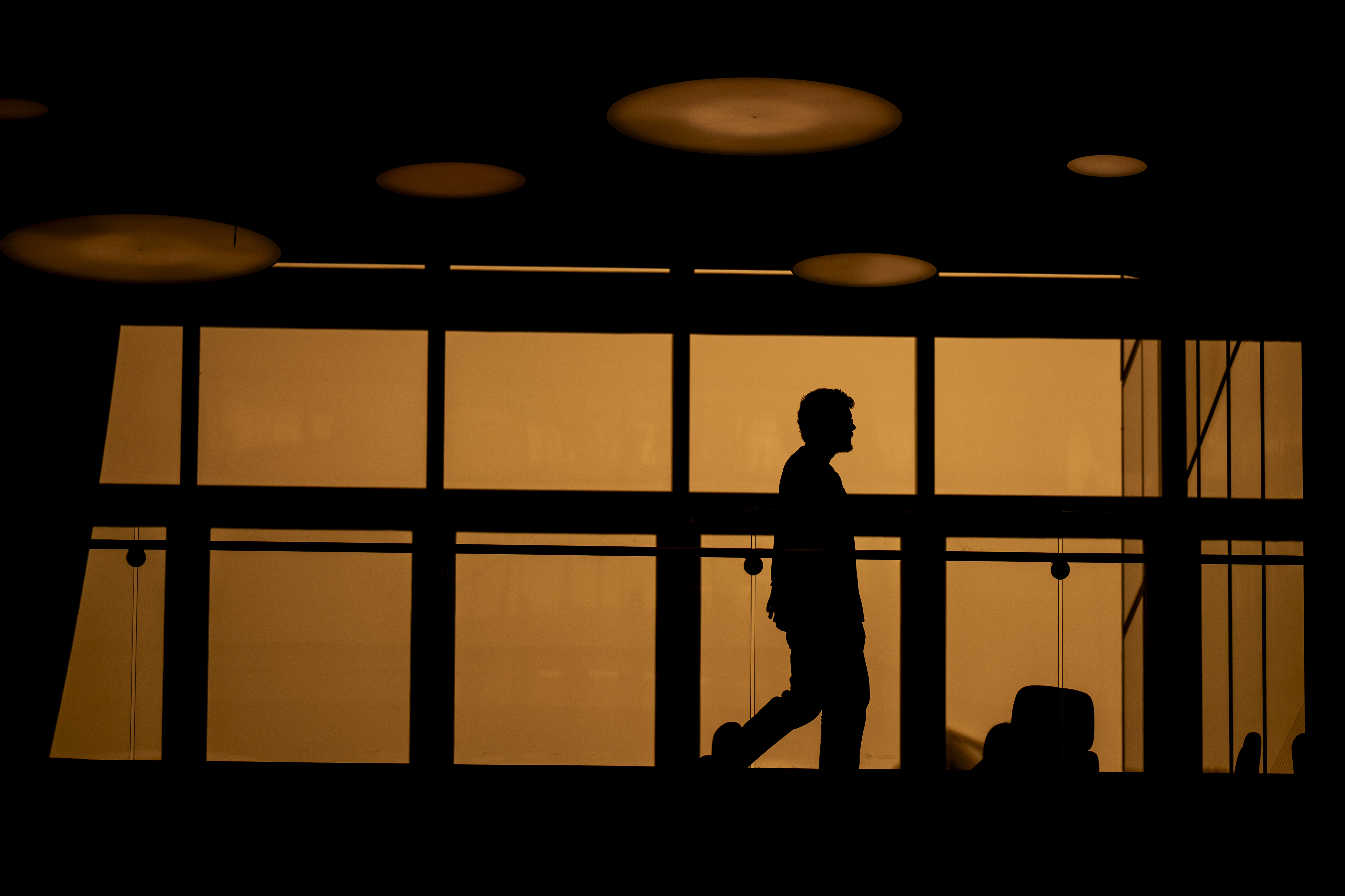 A person's silhouette is visible through orange-tinted windows inside a smoky-lit building.
