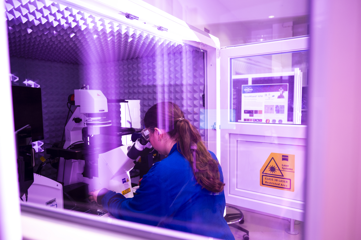 Samantha Finkbeiner peering through a microscope eyepiece inside an enclosed imaging chamber.