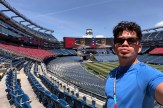 A student with a blue shirt and sunglasses photographs himself in the stands of the World Cup stadium.